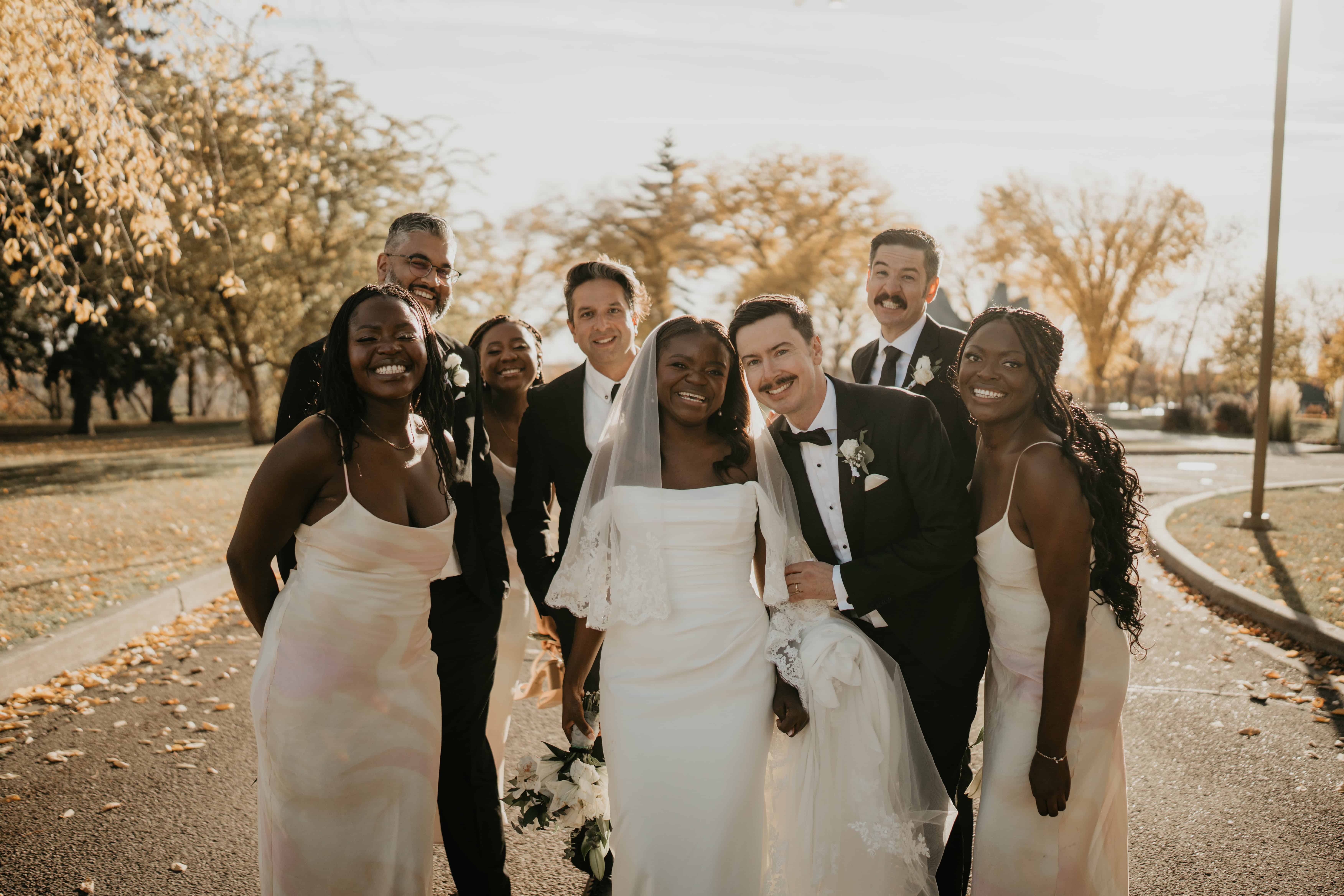 candid photo of a wedding party huddled together in the fall golden hour. Everyone is smiling with the bride and groom in the centre.